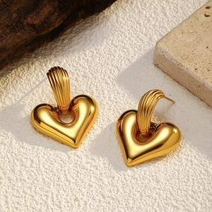 Detail of heart-shaped gold titanium steel earrings on a textured minimalist background