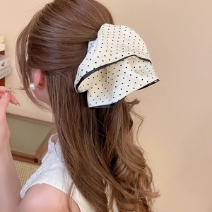 Detail of a large white hair scrunchie with black polka dots and elegant bow design