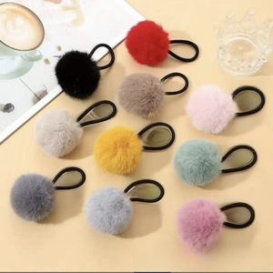 Flat lay of colorful faux fur pom pom hair ties in ten vibrant shades on yellow background