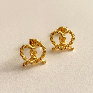 Detailed view of gold twisted rope heart stud earrings with butterfly backs on beige texture