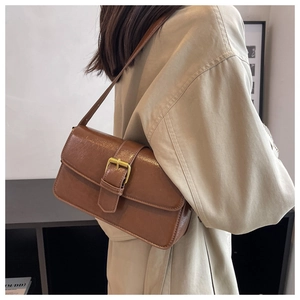 Detail of a brown glossy vintage shoulder bag with golden buckle on a beige trench coat