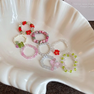 Detail of colorful beaded flower rings in a white shell dish with butterfly charms