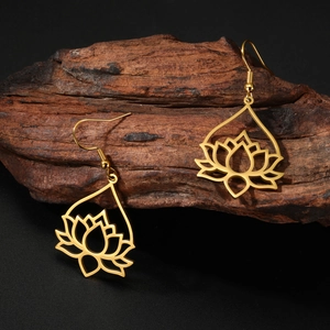 Macro shot of gold-plated lotus flower cutout earrings on a textured wooden block