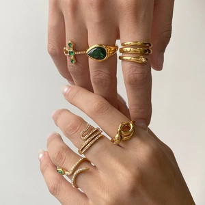 Close-up of luxury gold snake rings with green gemstones and zircon stones on hands