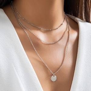 Close-up of triple-layered silver necklace featuring round pendant on female model