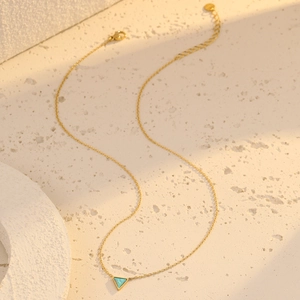 Golden stainless steel necklace with triangular turquoise pendant on a white stone surface