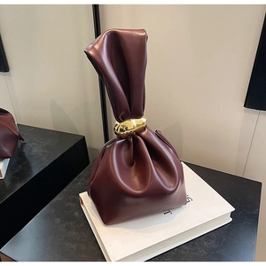 Detail of burgundy leather bucket bag with elegant golden metal buckle on books