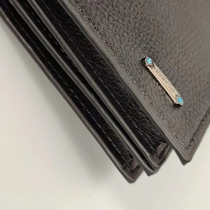 Detalle de billetera de cuero negro con borde de triple capa y logotipo de cristal azul