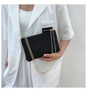 Detailed view of black evening bag with rhinestones and gold chain worn with white blazer