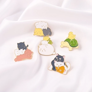 Detail of stacked cat enamel pins and duck on turtle brooch on white silk fabric