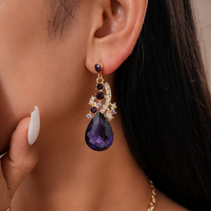 Detail of luxury teardrop earring with purple crystals and gold metal on female model