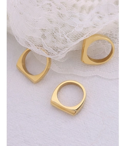 Close-up of three gold-plated square signet rings on a white lace background
