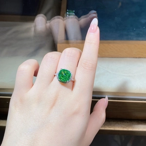 Close-up of radiant cut emerald ring on model finger with shimmering diamond halo