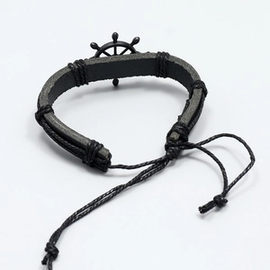 Close-up of black braided leather bracelet featuring a metallic ship wheel charm detail