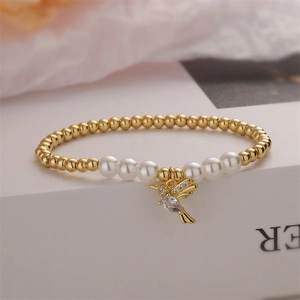 Close-up of a gold-beaded bracelet with white pearls and a crystal hummingbird charm
