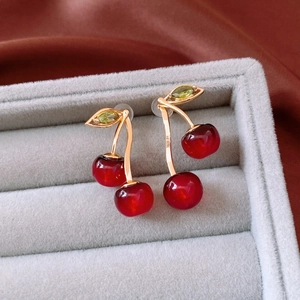Macro shot of cherry pendant earrings with red glass beads and green zircon leaves