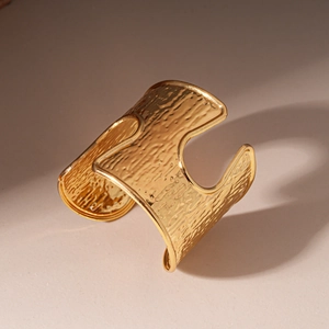 Detail shot of the wide gold cuff bracelet featuring a distinct hammered metal texture