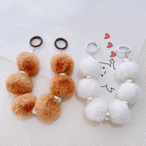 Detailed view of plush pompom phone charms with faux pearls and metal clips