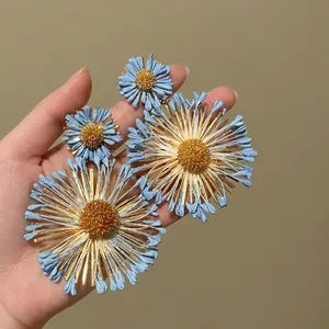 Macro shot of blue floral dangle earrings with gold petals and 3D textured matte finish