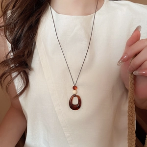 Détail du pendentif géométrique en acrylique ambré sur collier avec vêtement en lin