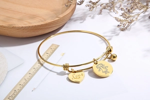 Detail of adjustable gold bangle with heart Love pendant and circular girl charm on wood