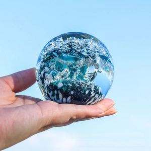 Macro shot of glass crystal ball with blue ocean waves and bubbles against blue sky