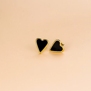 Minimalist gold-edged heart stud earrings with black enamel finish on beige background