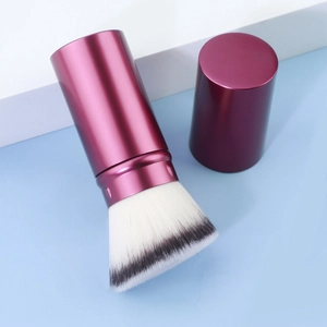 Detail of retractable makeup brush with rose red metallic handle and dense soft bristles
