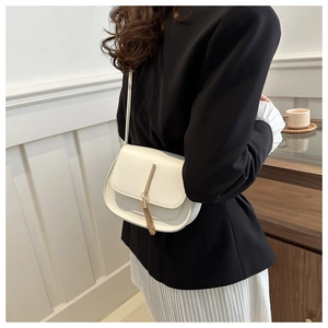 Detail shot of a minimalist cream saddle bag featuring a gold metal bar and elegant tassels