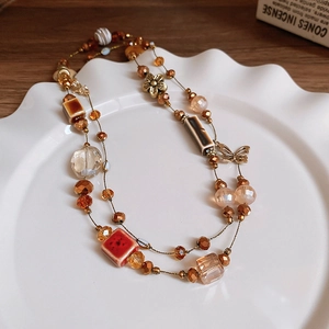 Detail of vintage beaded necklace with flower and butterfly charms on a white ceramic plate