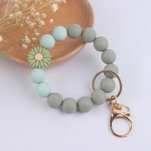 Macro detail of silicone bead bracelet keychain with daisy charm on a wooden tray