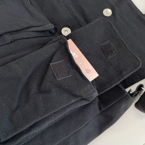 Detailed close-up of a black canvas crossbody bag with velcro pockets and metal snap buttons