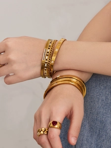 Détail de bracelets géométriques dorés et bagues cœur avec zircons sur un poignet