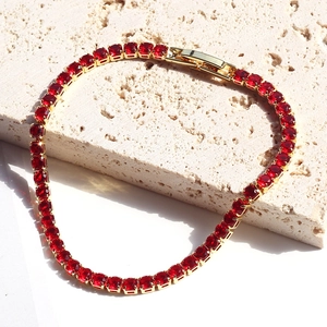 Elegant gold tennis bracelet featuring round-cut red zircons on a textured stone surface