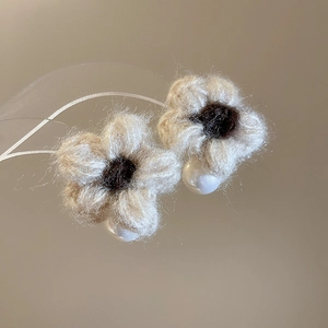 Macro detail of knitted flower earrings with plush petals and dangling white pearls