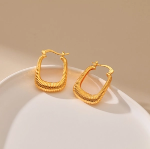 Chunky gold U-shaped hoop earrings with spiral ribbed texture on white ceramic tray