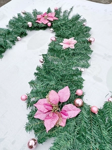Close-up of green candy cane-shaped Christmas garland with pink flowers and silver ornaments