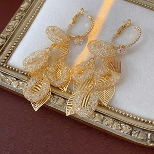 Dettaglio di orecchini a foglia dorata con zirconi su un elegante tessuto bianco