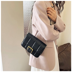 Detail of black quilted shoulder bag with gold chain strap on a pink blazer