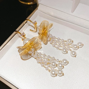 Macro detail of gold flower earrings with white pearl tassels on a jewelry box