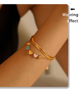 Detail view of a double-layered gold snake chain bracelet with colorful heart pendants