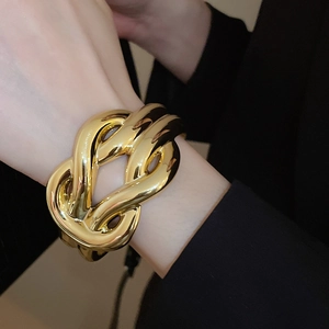 Close-up of polished gold knot bangle bracelet worn with a formal black sleeve