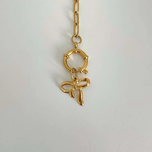 Detail showing a shiny gold bow pendant hanging from a circular clasp on a metal necklace