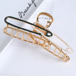 Detail view of a large gold metal hair claw clip with dark green and white enamel finish
