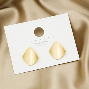 Matte gold geometric diamond stud earrings with silver post on luxury silk background