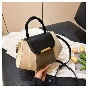 Detail of color-block shell bag with gold metal trim and detachable strap on leather chair
