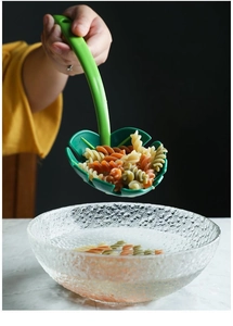 Leaf-shaped pasta strainer lifting rotini noodles from a clear bowl in a kitchen setting