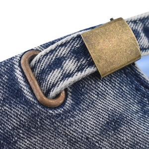 Macro shot of the adjustable bronze buckle on a washed blue distressed denim baseball cap