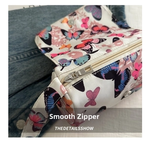 Detailed close-up of smooth silver zipper and butterfly print on white fabric handbag