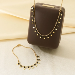 Detail of gold tassel necklace and bracelet set with black beads on beige silk fabric